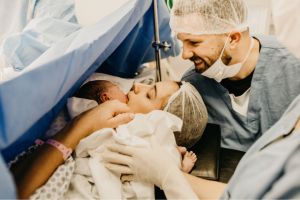 Une mère après un accouchement par césarienne qui embrasse son bébé avec le papa souriant